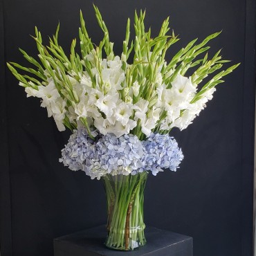 Generoso florero de gladiolas blancas rodeadas de hortensias