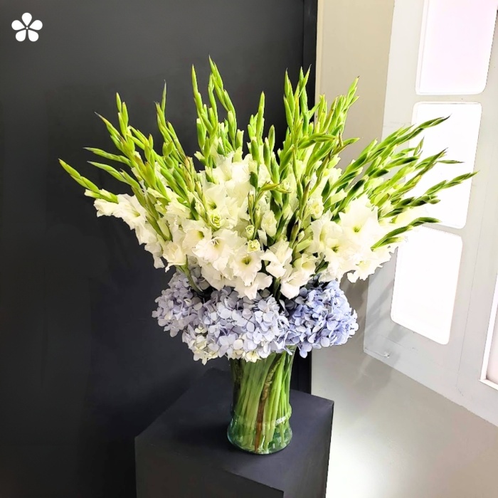 Generoso florero de gladiolas blancas rodeadas de hortensias
